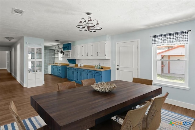 dining space with dark wood-style floors, baseboards, visible vents, a textured ceiling, and a chandelier