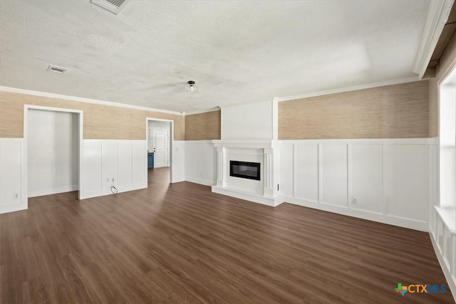 unfurnished living room with visible vents, a textured ceiling, a glass covered fireplace, dark wood finished floors, and wainscoting