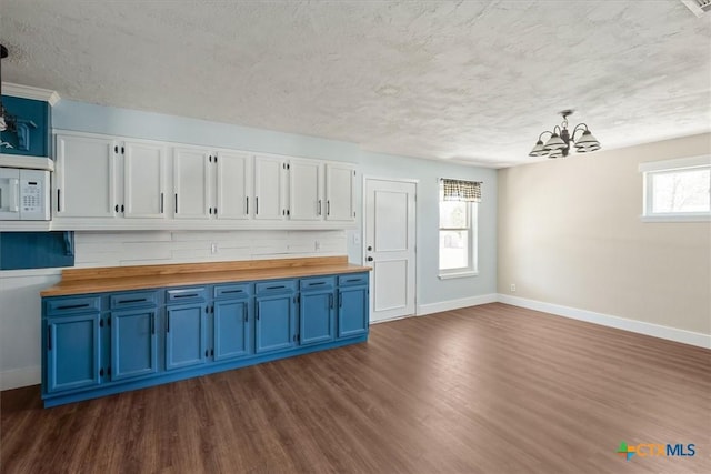 kitchen featuring white microwave, baseboards, dark wood-style flooring, butcher block countertops, and blue cabinets