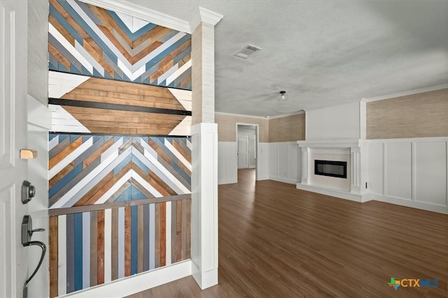 foyer featuring wood finished floors, a wainscoted wall, visible vents, a glass covered fireplace, and a decorative wall