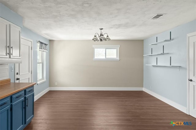 unfurnished dining area featuring visible vents, an inviting chandelier, baseboards, and dark wood-style flooring