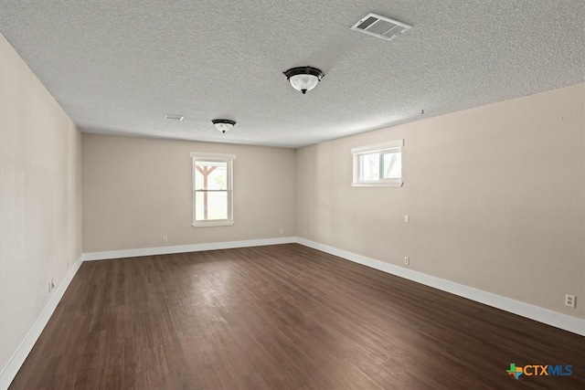 unfurnished room with dark wood finished floors, baseboards, visible vents, and a textured ceiling