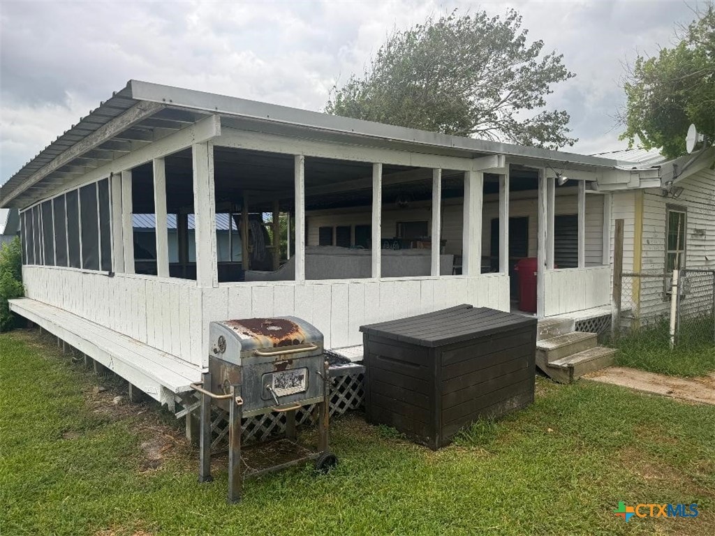 rear view of house featuring an outdoor fire pit, a lawn, and a sunroom