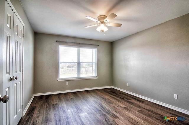 unfurnished room featuring dark wood-style floors, a ceiling fan, and baseboards