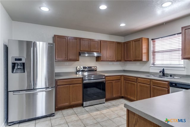 kitchen with under cabinet range hood, a sink, light countertops, appliances with stainless steel finishes, and brown cabinets