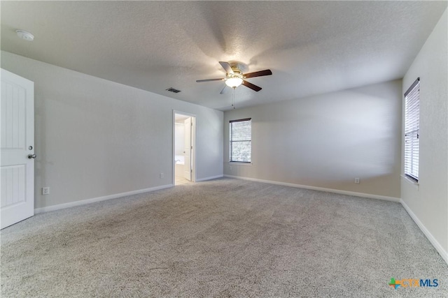 spare room featuring a textured ceiling, light colored carpet, a ceiling fan, baseboards, and visible vents