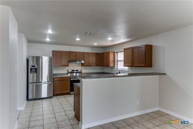 kitchen with stainless steel appliances, dark countertops, brown cabinetry, a peninsula, and under cabinet range hood