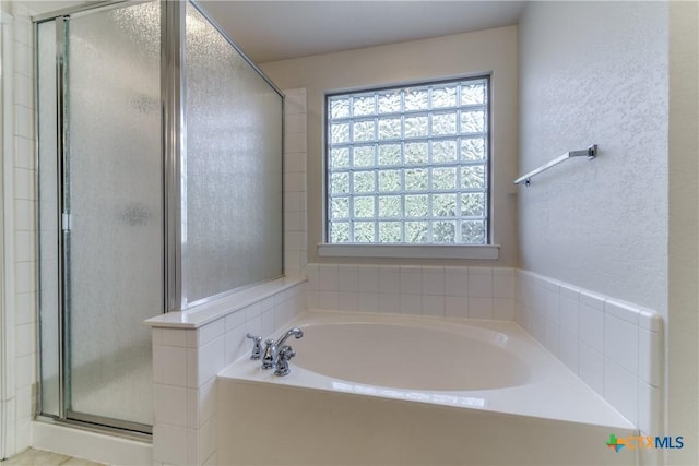 full bath with a textured wall, a garden tub, and a shower stall