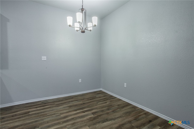 spare room featuring dark wood-type flooring and an inviting chandelier