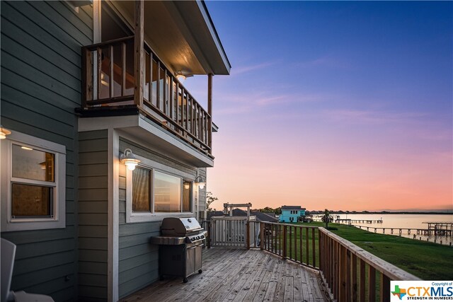 deck at dusk featuring a water view and grilling area