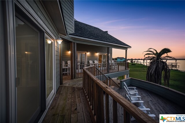 deck at dusk featuring a lawn and a water view