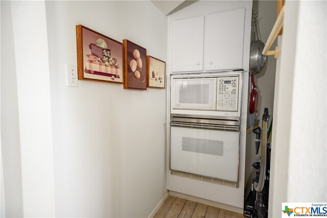 kitchen with white appliances, white cabinetry, and light hardwood / wood-style flooring