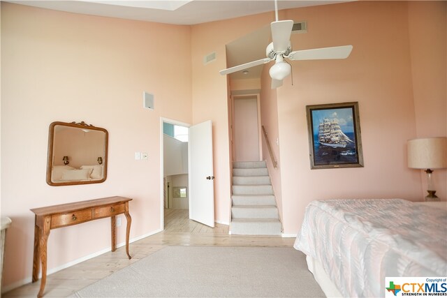 bedroom featuring light hardwood / wood-style floors, ceiling fan, and a towering ceiling