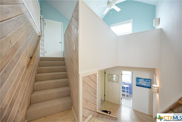 stairway with hardwood / wood-style floors, ceiling fan, and high vaulted ceiling