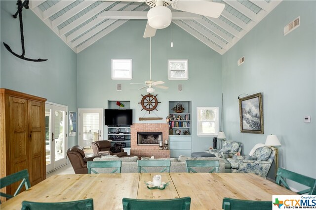 living room with high vaulted ceiling, beamed ceiling, a brick fireplace, and plenty of natural light