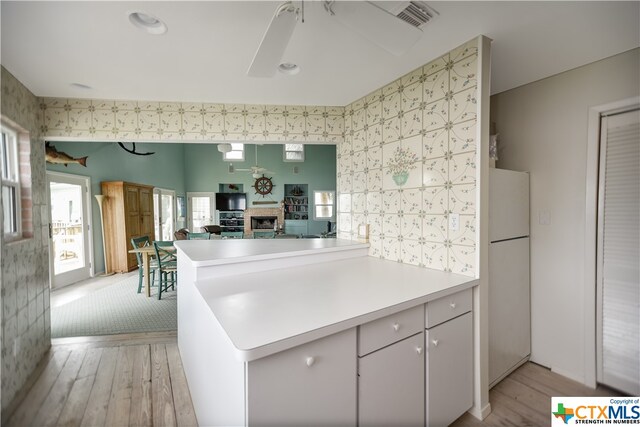 kitchen featuring a fireplace, light wood-type flooring, white refrigerator, white cabinets, and kitchen peninsula