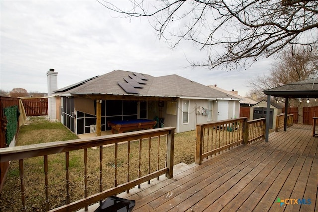 deck with a shed, a jacuzzi, a sunroom, and a lawn