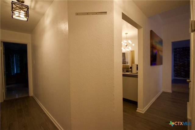 corridor with dark hardwood / wood-style floors and a chandelier