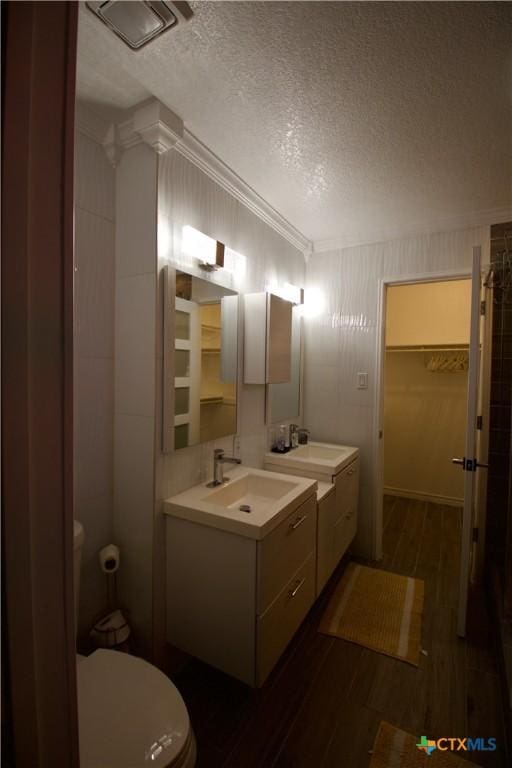 bathroom with crown molding, vanity, wood-type flooring, a textured ceiling, and toilet