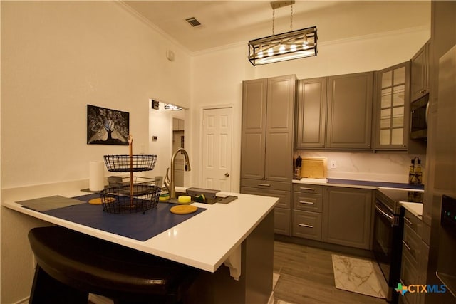 kitchen with a breakfast bar area, decorative light fixtures, electric range, ornamental molding, and dark hardwood / wood-style floors