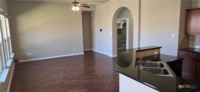 kitchen with baseboards, arched walkways, dark countertops, dark wood-type flooring, and a sink