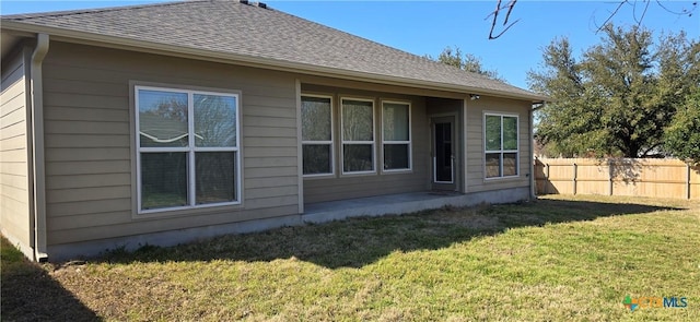 back of house featuring a shingled roof, fence, and a yard