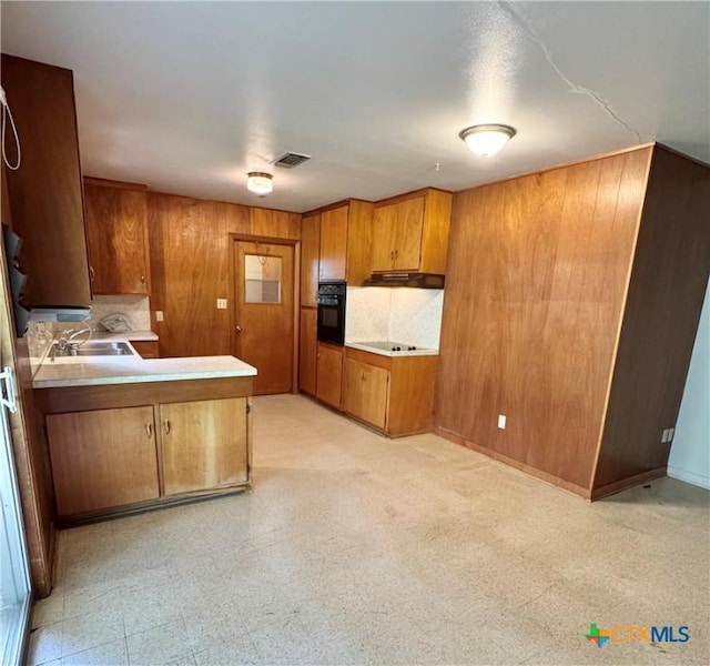 kitchen featuring black appliances, brown cabinetry, a sink, a peninsula, and wood walls