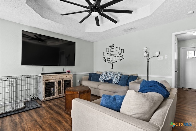 living room featuring ceiling fan, a tray ceiling, dark hardwood / wood-style floors, and a textured ceiling