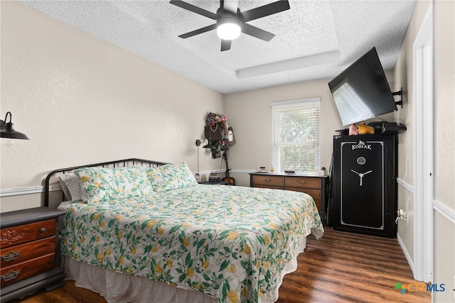 bedroom featuring dark hardwood / wood-style floors, a textured ceiling, ceiling fan, and a tray ceiling