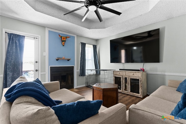 living room with dark wood-type flooring, ceiling fan, a tray ceiling, and a textured ceiling