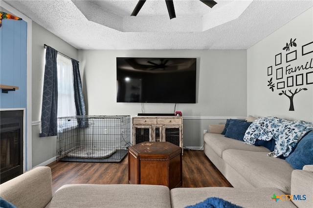 living room with a tray ceiling, a textured ceiling, dark hardwood / wood-style floors, and ceiling fan