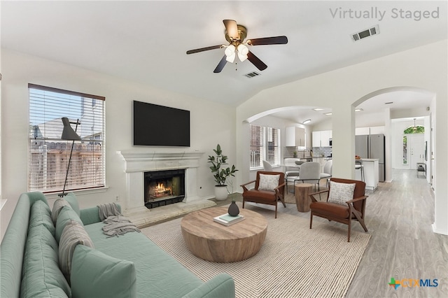 8430 Alvin High Ln, Austin, TX 78729 - living room with a ceiling fan, light wood-style floors, vaulted ceiling, arched walkways, and a warm lit fireplace