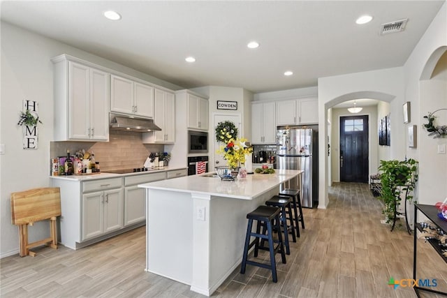 4032 Wild Bloom Rd, Seguin, TX 78155 - kitchen featuring black appliances, under cabinet range hood, arched walkways, a kitchen bar, and tasteful backsplash