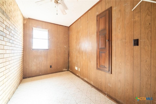 spare room featuring ceiling fan, wooden walls, and brick wall