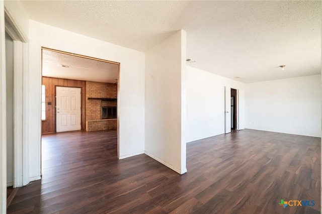 empty room featuring dark wood-type flooring, a textured ceiling, and a brick fireplace