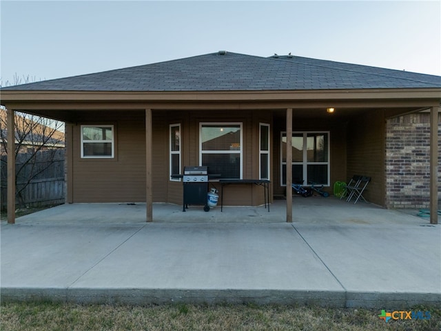 back of property featuring brick siding, a patio, and roof with shingles