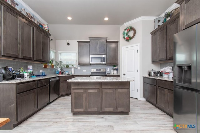 kitchen with light stone counters, a center island, appliances with stainless steel finishes, and dark brown cabinetry