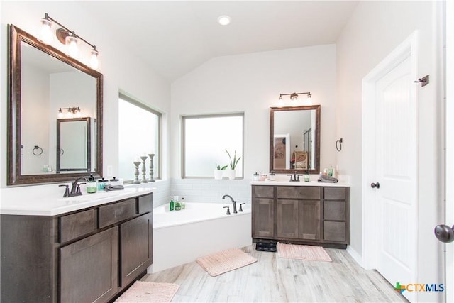 bathroom with a tub to relax in, vaulted ceiling, vanity, and wood-type flooring