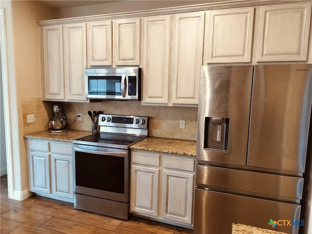 127 Augusta Dr, Wimberley, TX 78676 - kitchen featuring appliances with stainless steel finishes, decorative backsplash, light stone counters, light wood-type flooring, and baseboards