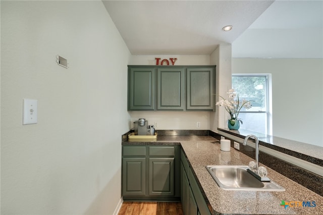 kitchen with wood finished floors, green cabinetry, a peninsula, recessed lighting, and a sink