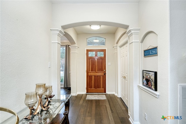 foyer featuring dark wood-type flooring, decorative columns, baseboards, and arched walkways