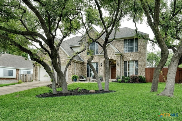 traditional-style house with brick siding, fence, roof with shingles, a front yard, and driveway