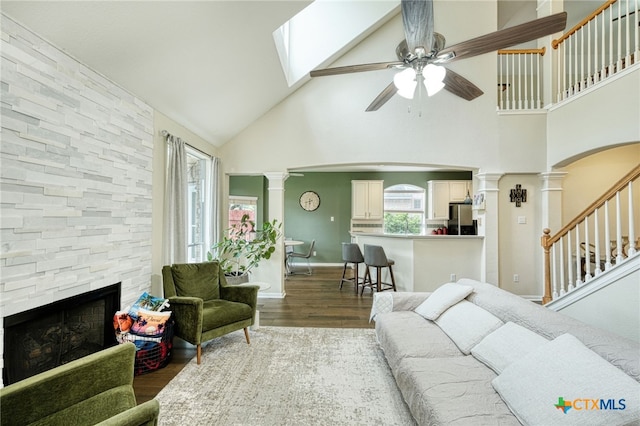 living area featuring a ceiling fan, wood finished floors, high vaulted ceiling, decorative columns, and a fireplace