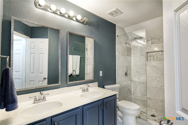 bathroom with a tile shower, visible vents, toilet, and a sink