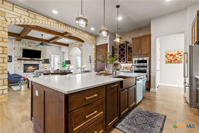 kitchen with stainless steel appliances, a center island with sink, sink, a fireplace, and light hardwood / wood-style flooring