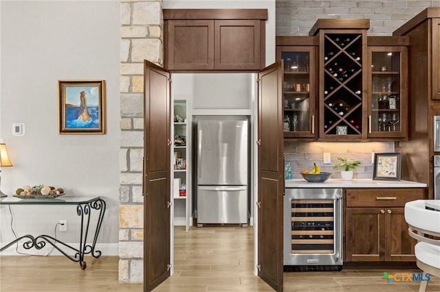 bar featuring light hardwood / wood-style floors, stainless steel refrigerator, wine cooler, and backsplash