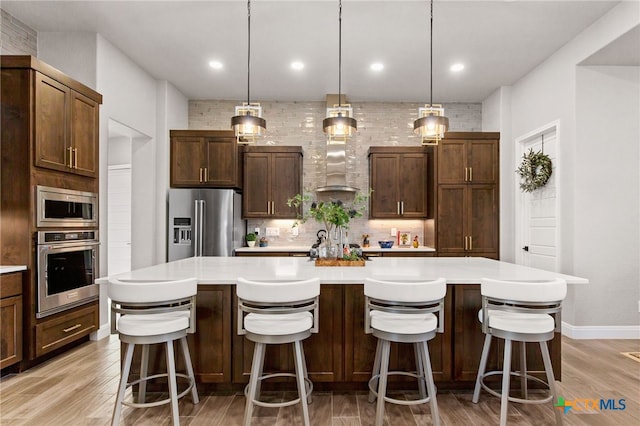 kitchen featuring a large island with sink, a breakfast bar, appliances with stainless steel finishes, and decorative light fixtures