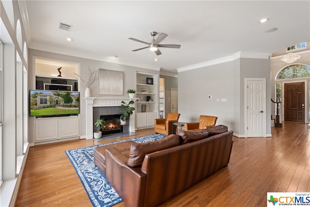 living area with light wood finished floors, a lit fireplace, built in features, and crown molding