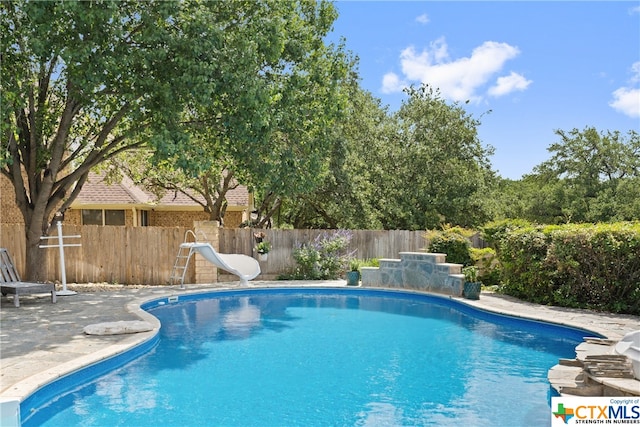 view of swimming pool with a fenced in pool, fence, a water slide, and a patio