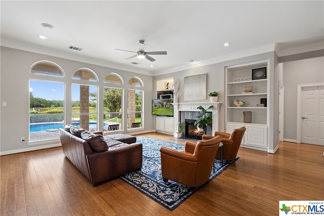 living area with built in shelves, a high end fireplace, visible vents, and hardwood / wood-style flooring